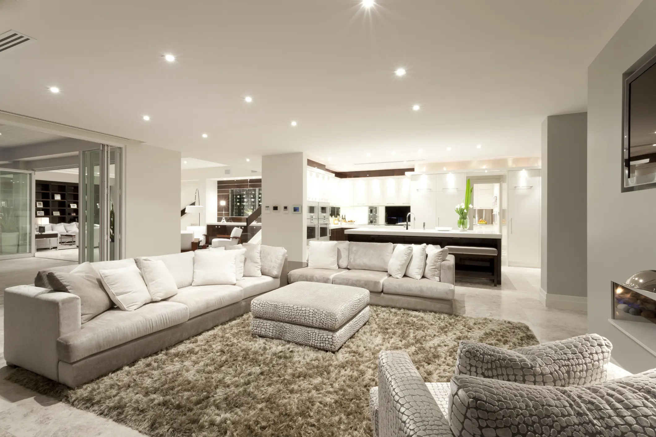 Cozy living room with spacious sofas Modern spacious living room with white sofas, an ottoman, and a textured rug under bright recessed lighting.