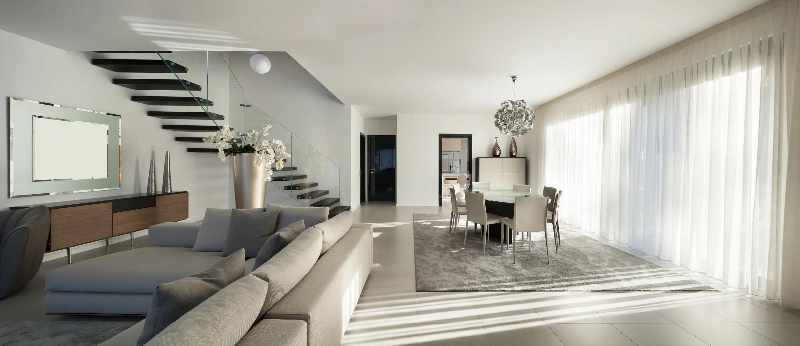 beautiful apartment, interior Modern living room with a beige sectional sofa, floating staircase, dining area with chandelier, and neutral color palette.