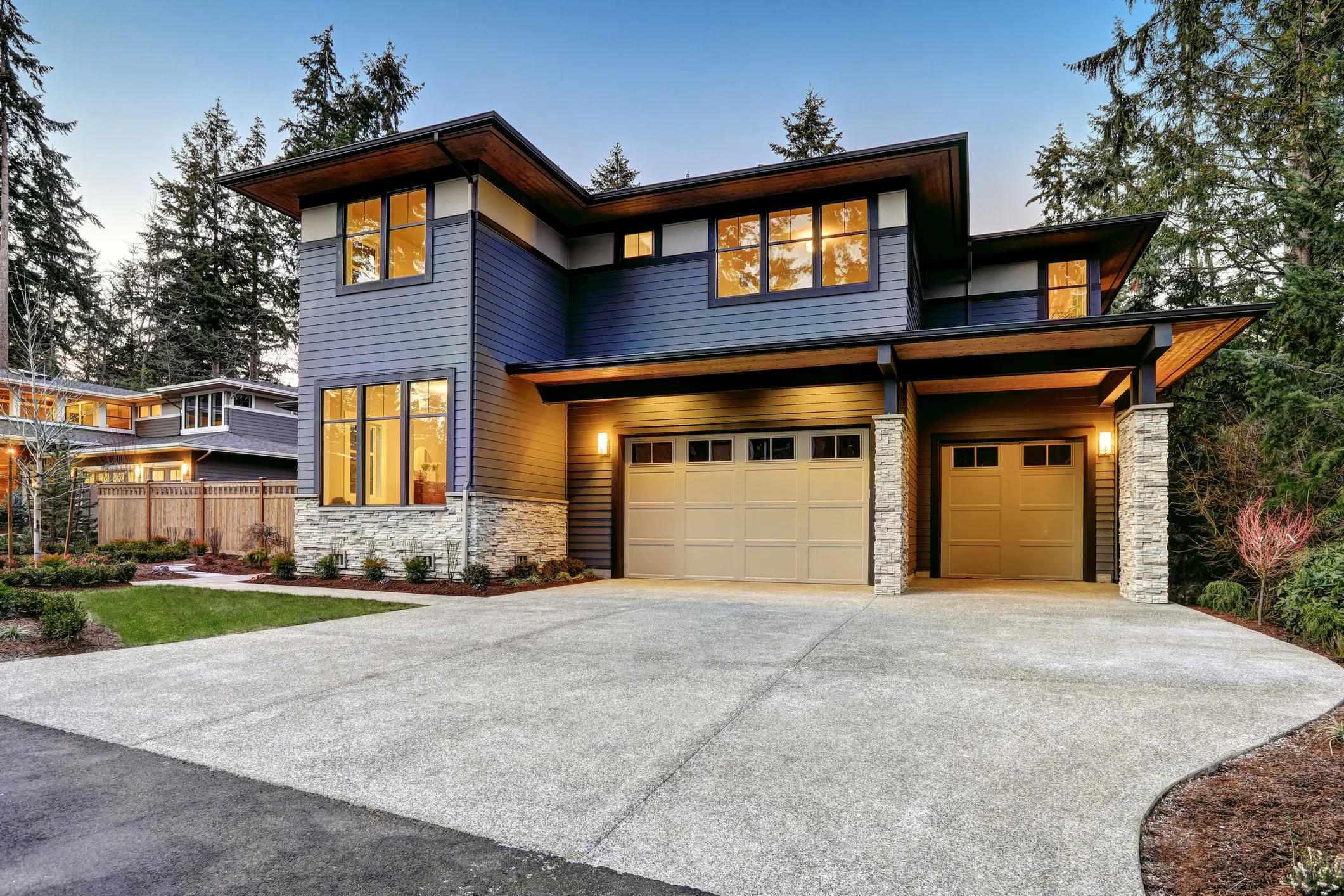 Modern two-story house with large windows and a spacious driveway in the evening light.