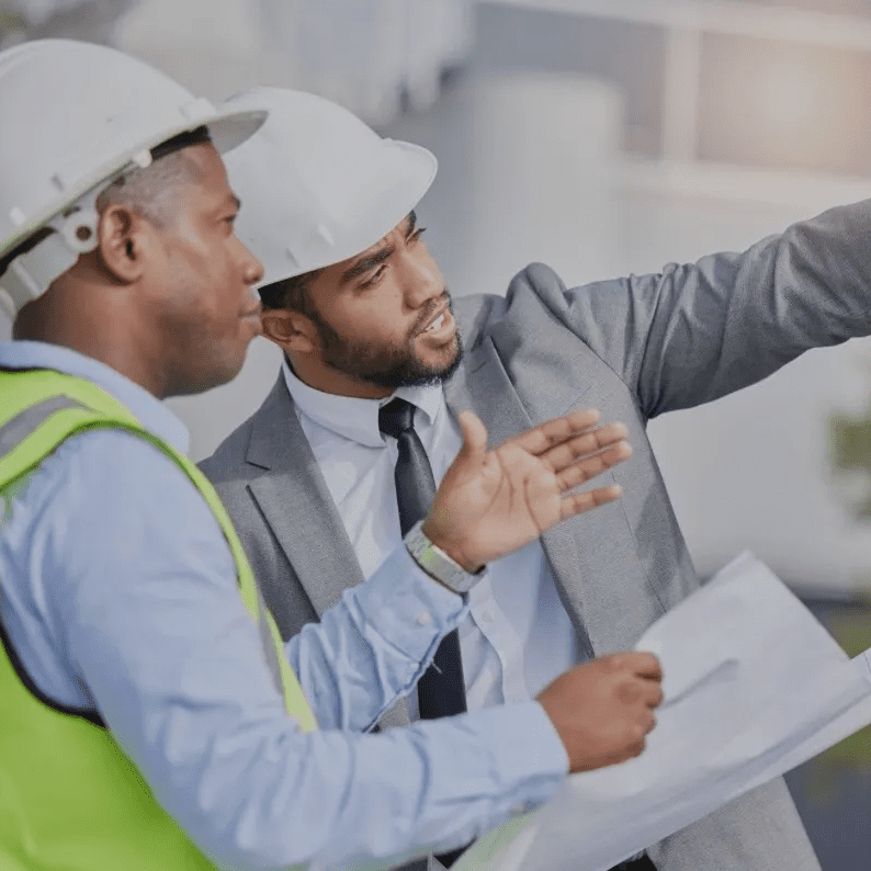 Two construction workers in helmets reviewing plans, discussing details on a building site.
